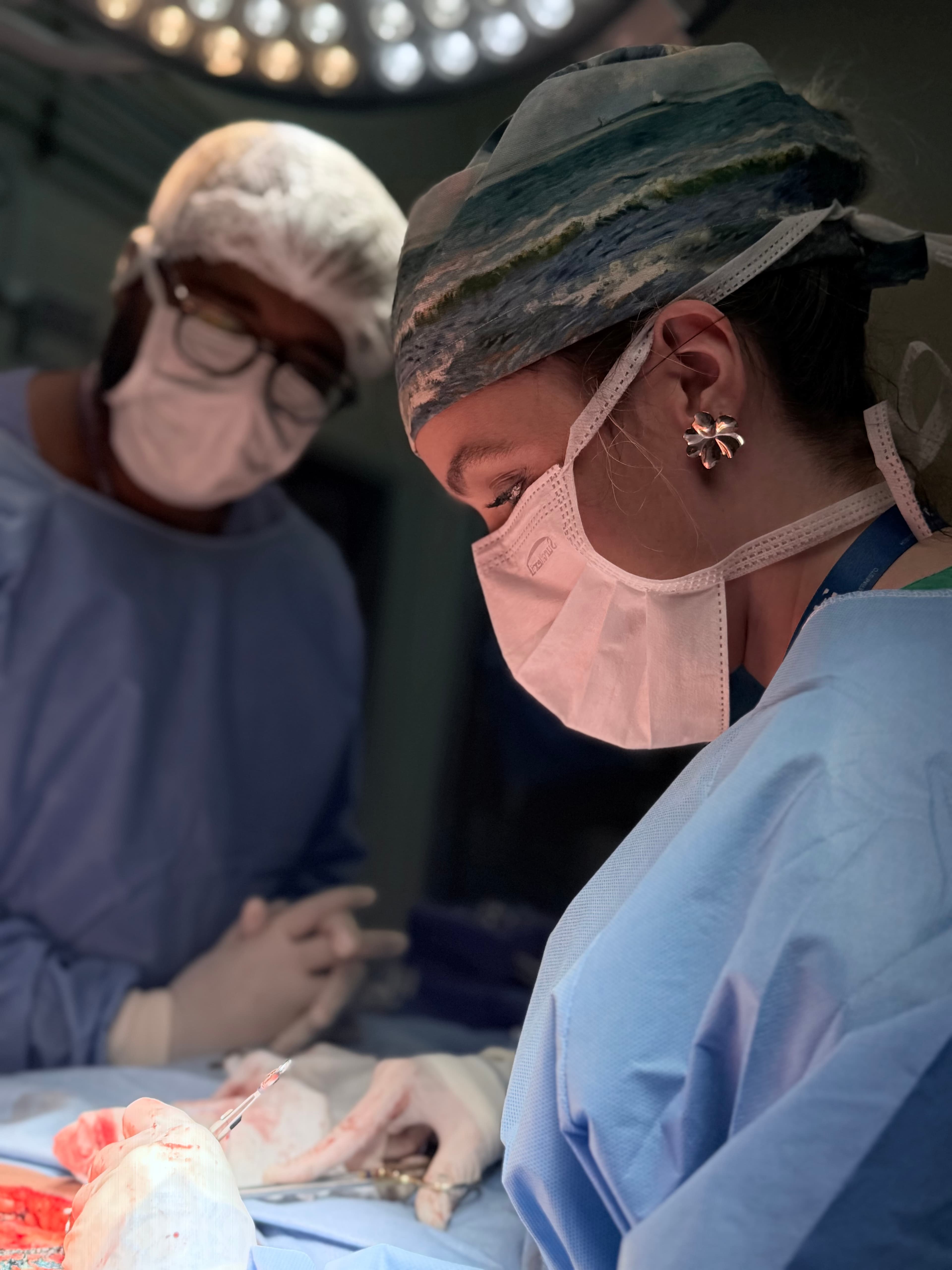 Cirurgiã concentrada opera paciente sob luzes brilhantes, acompanhada por colega em ambiente hospitalar estéril.